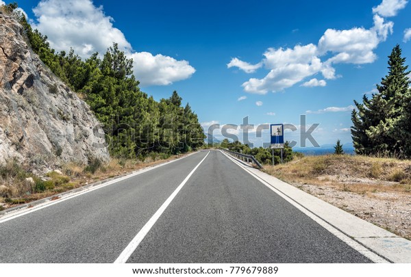 Asphalt road\
to the sea. Asphalt highway in a sunny day outside the city passing\
through the cliff next to the\
sea.