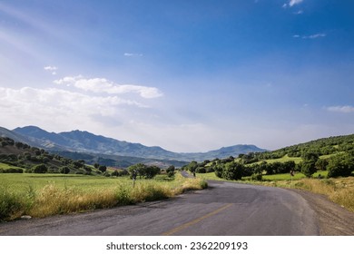 Asphalt road in summer season with traffic signs. An abandoned road in the city of Kurdistan, Iran. A beautiful road in the middle of the meadow with a view of the mountains on a sunny day. blue sky.