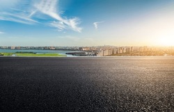 Asphalt Road And Urban Skyline With Lake At Sunset