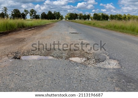 Asphalt road with a very large and deep pothole. Pothole is half filled with water. 