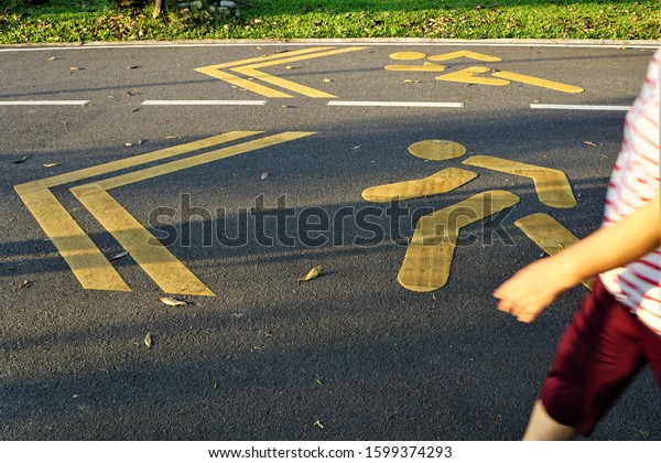 Asphalt road with white dash that is divided into\
two sides.There have yellow arrow-shaped symbol. One side has a\
graphic of a person running,the other has walking symbal with\
blurrred walking\
person.