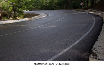 
An Asphalt Road In A Winding Down Forest. Curved. 
There Is A Traffic Sign. No People.