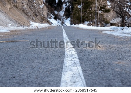 Asphalt road in winter mountains with bright white unbroken line as road marking (single continuous line). Winter view of empty mountain road with marking in Kazakhstan. White solid line road marking.