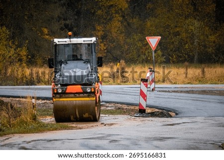 Asphalt roller machine working on road construction site in autumn, heavy equipment paving new countryside road, infrastructure and engineering concept