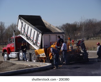 Asphalt spreader being filled by a dump truck.