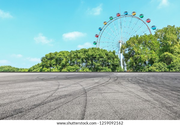 Asphalt square road and ferris wheel with green\
forest landscape