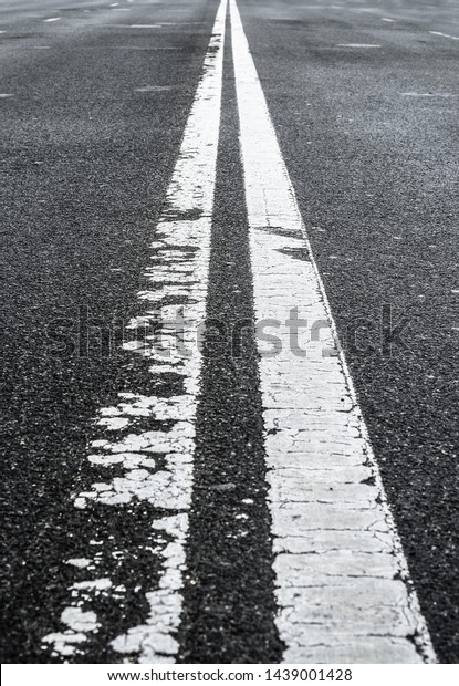 Asphalted road with two\
continuous faded white strips. White road divider lines of a\
highway. Long banner format. Two-way asphalt road, close up of the\
dividing road strip.