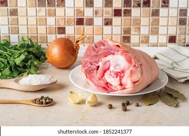 Aspic Or Jellied Meat Raw Ingredients: Pork Leg Shank On A Plate, Onion, Garlic, Salt, Pepper, Parsley And Bay Leaves On The Kitchen Table. Homemade Food Recipe. Front View. 