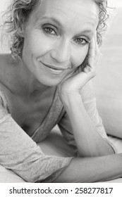 Aspirational Black And White Beauty Portrait Of An Attractive Mature Healthy Woman Laying Down On A White Sofa At Home, Smiling And Relaxing Indoors. Home Living And Well Being Lifestyle.