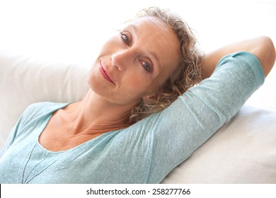 Aspirational Close Up Beauty Smiling Portrait Of An Attractive Mature Healthy Woman Laying Down On A White Sofa At Home, Being Thoughtful And Relaxing Indoors. Home Living And Well Being Lifestyle.