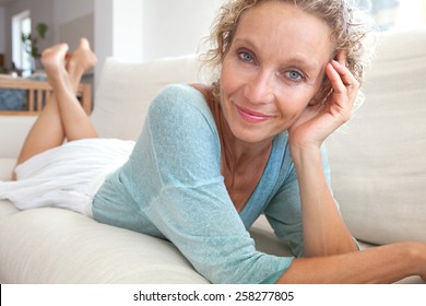 Aspirational Close Up Beauty Smiling Portrait Of An Attractive Mature Healthy Woman Laying Down On A White Sofa At Home, Being Thoughtful And Relaxing Indoors. Home Living And Well Being Lifestyle.