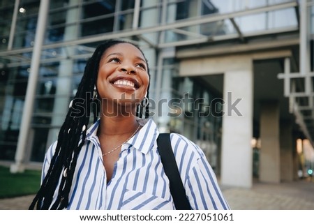 Aspiring young businesswoman smiling and looking away while commuting in the city. Happy young business woman listening to music on her way to the office in the morning.