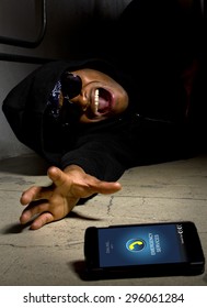 Assaulted Gangster Calling For Help Or Medical Emergency With A Cell Phone. On The Foreground Is A Cell Phone He Was Using To Call 911.  He Is Laying On The Ground Injured.