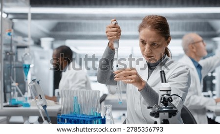 Assay development specialist in lab pipetting blue liquid into test tube to analyze it. Molecular biologist transferring chemical sample to prepare for immediate spectroscopic analysis, camera B
