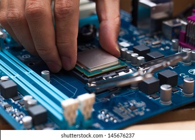 Assembling high performance personal computer, inserting CPU, processor into the motherboard socket, opened PC case in background, shallow depth of field, focus on hand