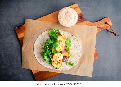 Assembling a Roasted Vegetable and Halloumi Wrap: A whole wheat flatbread topped with roasted vegetables, hummus, halloumi cheese, and harissa sauce