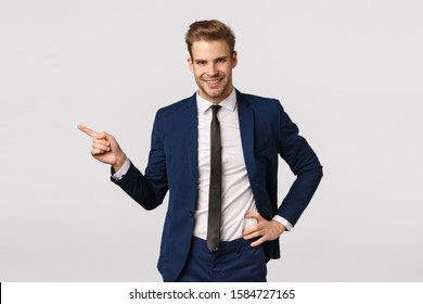 Assertive Charismatic Blond Businessman With Bristle, Wear Classic Suit, Pointing Left And Smiling Camera, Telling About Great Product, Advertise Financial App, Business Concept, White Background