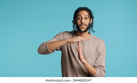 Assertive Middle Eastern man asking for timeout, doing hand gestures. BIPOC person doing pause sign gesturing, wishing for break, isolated over blue studio background, camera A