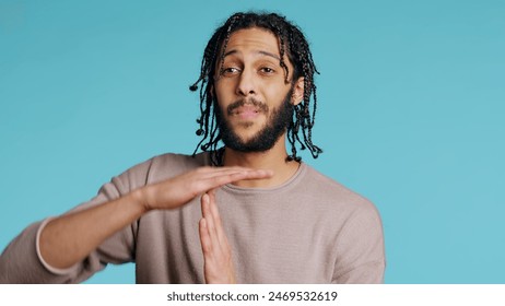 Assertive Middle Eastern man asking for timeout, doing hand gestures. BIPOC man doing pause sign gesturing, wishing for break, isolated over blue studio background, camera B