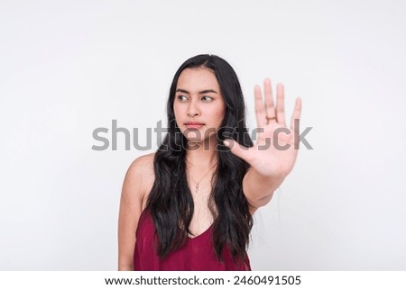 Assertive young Asian lady in chic maroon dress, telling someone she's not interested while looking away. Isolated on a clean white background.