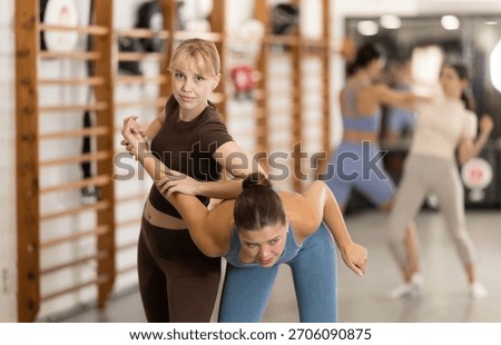 Assertive young female trainee applying armlock technique on person in sports hall