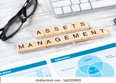 Asset Management Concept With Letters On Cubes. Still Life Of Office Workplace With Supplies. Flat Lay Vintage Wooden Desk With Computer Keyboard And Analytic Report. Capital Investment Company