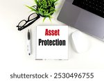 Asset protection text on notepad with laptop, glasses, plant, and pen on white desk. 