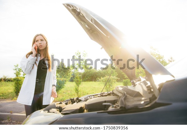 assistance on the
road - worried woman standing in front of broken car, looking at
engine and calling for
help