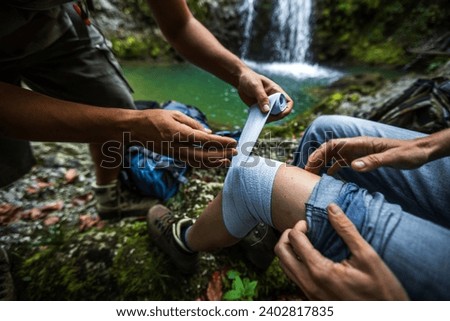 Assistance of a Woman Thigh With an Elastic Medical Bandage from First Aid Travel Kit on a Hike in Wilderness