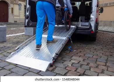 Assistant Helping Disabled Person On Wheelchair With Transport Using Accessible Van Ramp