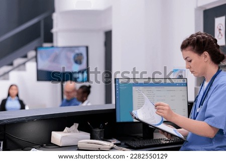 Assistant holding clipboard reviewing the patients medical history before their appointment, working in hospital waiting area. Nurse looking at patient symptoms planning health care treatment