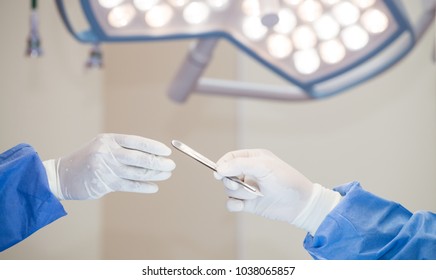 Assistant in medical glove holding a scalpel sending to surgeon hand for starts operate in operating room,Real surgery team in the operating room,Surgeons performing surgery in operating theater, - Powered by Shutterstock