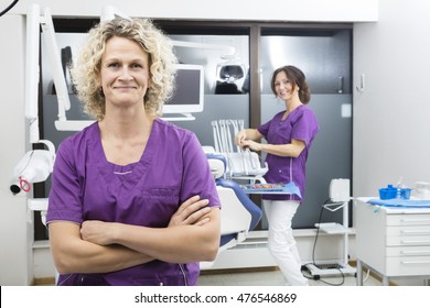 Assistant Standing Arms Crossed With Colleague Working In Dentis