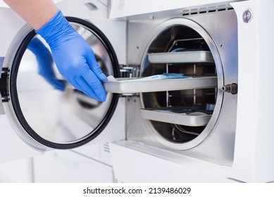 Assistant's hand in gloves insert packaged dental instrument to the autoclave to sterilise. - Shutterstock ID 2139486029