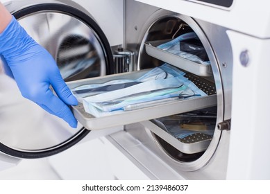 Assistant's hand in gloves insert packaged dental instrument to the autoclave to sterilise. - Shutterstock ID 2139486037