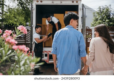 Assisted by a professional delivery team a couple transitions to their new home. Together they unload and lift cardboard boxes ensuring an organized and efficient move. Moving Day Concept - Powered by Shutterstock