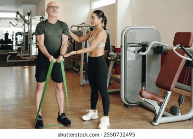 Assisting Senior Man with Resistance Band Exercises in Gym - Powered by Shutterstock