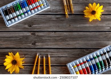 Assorted Art Supplies on Wooden Background. A flat lay of assorted art supplies on a rustic wooden background, featuring watercolor paint tubes, paintbrushes, yellow pencils, and vibrant yellow - Powered by Shutterstock