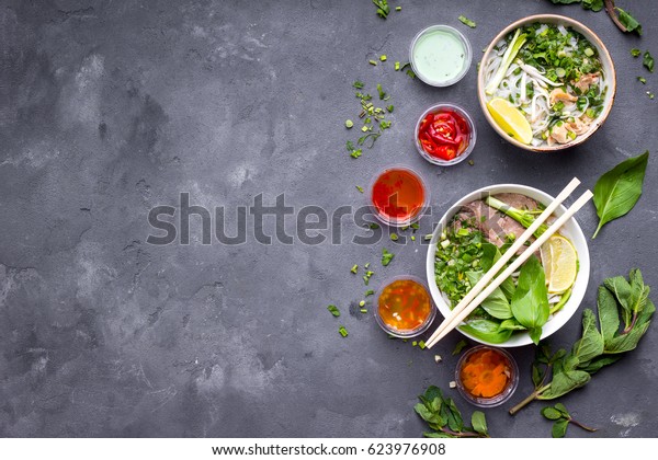 Assorted asian dinner\
with vietnamese noodle soup pho bo, pho ga, spring rolls, vegetable\
salad, copy space