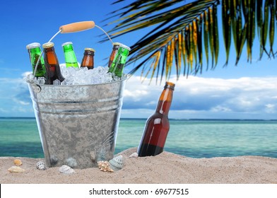 Assorted Beer Bottles In A Bucket Of Ice And One In The Sand On A Tropical Beach. 