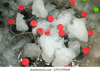 Assorted Bottled Beverages Rotating in Ice. Multiple glass bottles with colorful caps cooling in an ice-filled mixing display. Summer refreshment and beverage retail concept.
