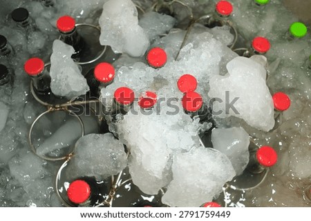Assorted Bottled Beverages Rotating in Ice. Multiple glass bottles with colorful caps cooling in an ice-filled mixing display. Summer refreshment and beverage retail concept.