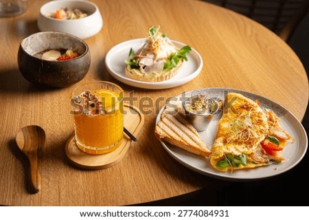 Assorted brunch dishes and fresh drinks served on a wooden table in a modern cafe environment. Stylish and contemporary food photography featuring a wide variety of breakfast and lunch meals including sandwiches, toast, salad, desserts, cake, sweets, pastries, cocktails and fresh orange juice. Bright natural light enhances textures, colors and fine details of the scene, creating an inviting, warm and appetizing atmosphere. Aesthetic composition with carefully arranged plates, elegant serving style and a balance of healthy, organic and gourmet options. Concept of brunch culture, relaxed dining, cafe lifestyle, social gathering and modern urban living. Ideal visual for themes such as restaurant menu design, blog content, culinary inspiration, hospitality industry, premium dining experience, lifestyle branding and social media marketing. The scene captures a cozy yet professional setting with vibrant ingredients, fresh herbs, fruits and visually appealing plating presentation. Perfect for advertising campaigns, digital marketing, editorial publications, website backgrounds, banners and promotional materials. Includes copy space for text placement, with both top view and close up perspectives highlighting freshness, quality and variety of dishes. The composition reflects current global trends, clean eating habits, balanced meals and premium cafe presentation style. Suitable for illustrating concepts of breakfast time, lunch break, weekend brunch, friendly meeting, casual dining experience, morning routine and food enjoyment. High detail image emphasizing textures, layers, colors and contrast of ingredients, making it visually engaging, attractive and commercially versatile. Focus on freshness, quality ingredients, modern plating and natural presentation, evoking comfort, taste and a high-end cafe experience.