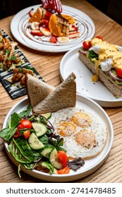 Assorted brunch table featuring fried eggs appetizers and fruit cake. High angle view of brunch spread with eggs, toast, seafood appetizers, and a fruit-covered sponge cake.