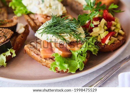 assorted bruschetta with different fillings on a plate in a restaurant. Small sandwiches of toasted bread, vegetables and fish. Snacks for the buffet