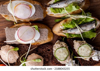 Assorted Bruschetta With Rabbit Liver, Cod Liver, Tulle On Lettuce And Cucumber Slices. On Top Of The Bruschetta Are Pea Microgreen Sprouts. Bruschetta Lie On A Wooden Board, The Board Stands On A Woo