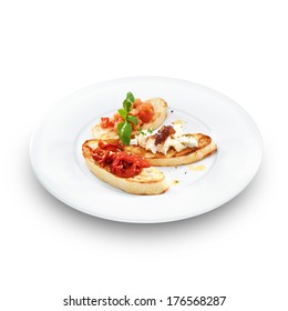 Assorted bruschetta with salmon, air-dry tomatoes or goat cheese served with the basil leaf on a round white plate isolated on white. 