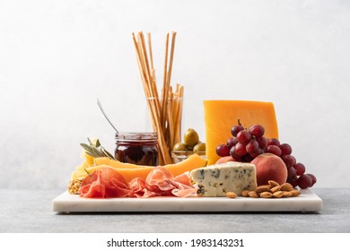 Assorted cheese, ham, fruit, jam, bread sticks, nuts. Cheese platter. Marble tray on table covered with linen tablecloth. Side view  - Powered by Shutterstock