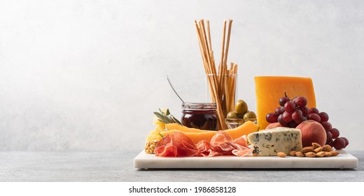 Assorted cheese, ham, fruit, jam, bread sticks, nuts. Cheese platter. Marble tray on table. Side view  - Powered by Shutterstock