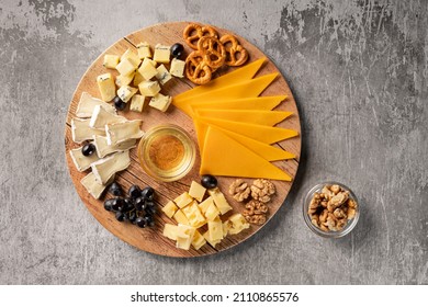 Assorted Cheese On A Wooden Plate On A Gray Background With A Copy Space. Top View Of A Wine Appetizer With Honey, Grapes, Pretzels And Walnuts On A Round Platter. Horizontal Orientation, No People